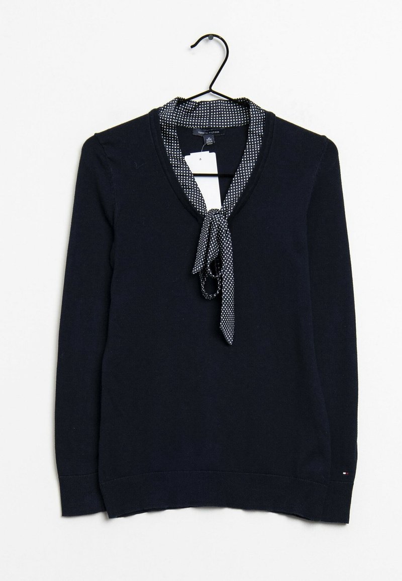 Pull bleu marine à manches longues avec un foulard à pois noué au niveau de l'encolure, suspendu sur un cintre noir sur fond blanc.