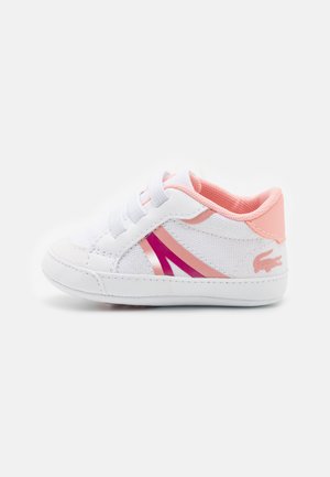 Weiße Sneaker mit pinken Akzenten, Schnürdesign, strukturiertem Canvas-Material und kontrastierenden Streifen an der Seite mit einem Logo.
