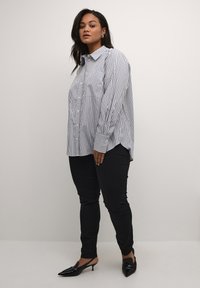 Gestreepte button-up shirt in wit en marineblauw, met een klassieke kraag en lange mouwen, gecombineerd met zwarte slim-fit broek en puntige flats.