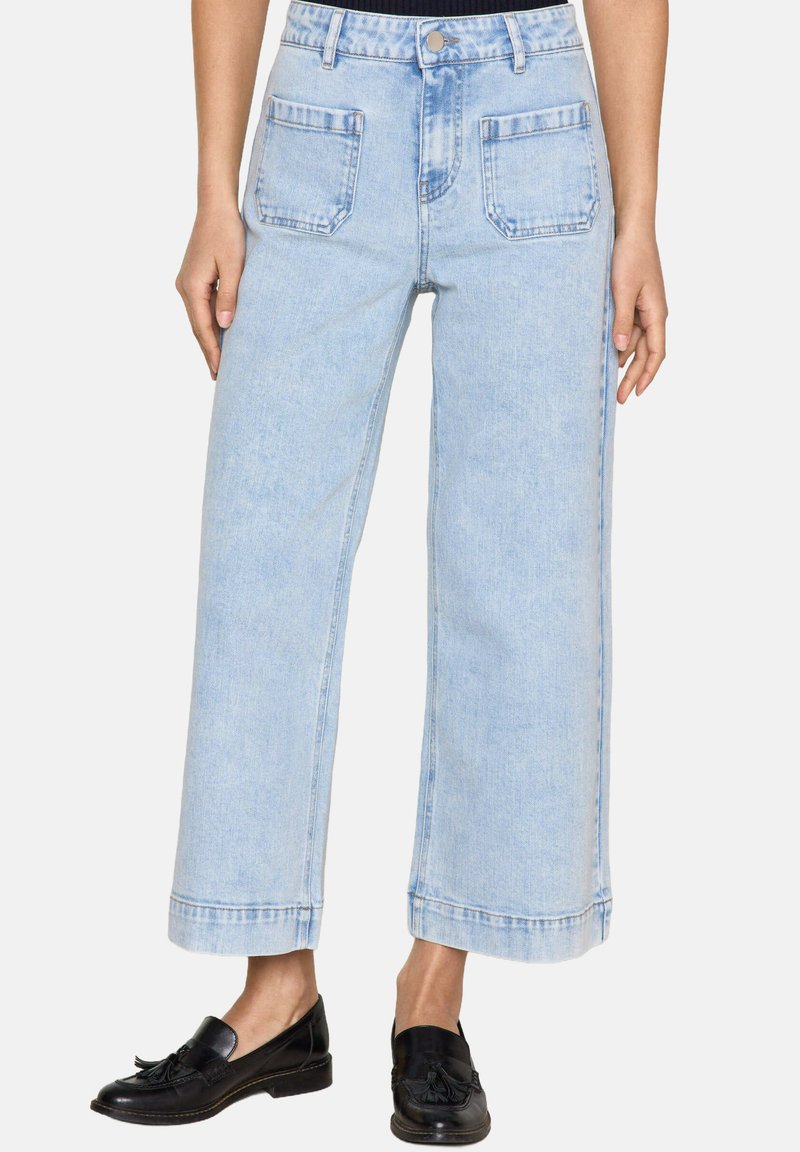 Pantaloni in denim azzurro chiaro a gamba larga con vita alta, cinque tasche e orlo grezzo. Il tessuto ha una superficie liscia e leggermente ingrassata.