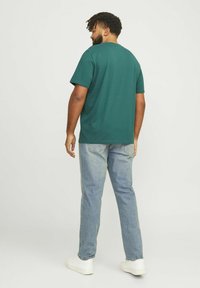 Groene katoenen T-shirt met een ronde hals, korte mouwen en een relaxte pasvorm. Gecombineerd met lichtblauwe spijkerbroek en witte sneakers.