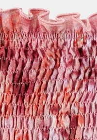 Texturovaná růžová a červená látka se sbíraným smokováním a řaseným okrajem, zobrazující detailní šití a barevné variace.