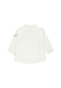 Camicia bianca a maniche lunghe con colletto, polsini abbottonati e una piccola toppa di un animale sulla manica sinistra. Tessuto liscio con una vestibilità comoda.