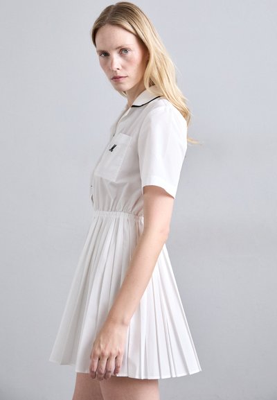 Hvit plissert kjole med korte ermer, krage og lomme detaljer. Stoffet ser glat ut, med samlet midje for en vidde silhuett.