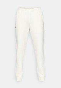 Krämfärgade sweatpants i mjukt material. Har ett elastiskt midjeband, sidfickor och en grön logotypdetalj på vänster lår.