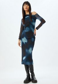 Robe midi à motif abstrait bleu avec de longues manches transparentes et un décolleté off-shoulder, portée avec des bottes plateforme noires.