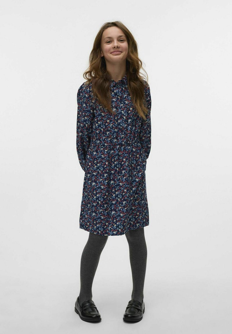 Abito a stampa floreale in blu navy con colletto con bottoni e vita elastica. Collant grigi e mocassini neri completano l'outfit.