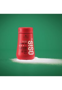 Contenant rouge de Schwarzkopf OSiS+ Dust It, une poudre volumisante matifiante. Présente une texture lisse, une forme arrondie, avec de la poudre blanche autour.