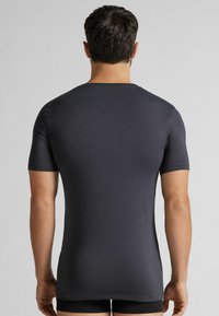 Czarna szara koszulka z krótkim rękawem o gładkim, dopasowanym kroju i okrągłym dekoltem. Materiał wydaje się lekki i elastyczny.