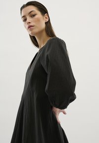 Abito nero con una superficie testurizzata, maniche lunghe a sbuffo e scollatura a V profonda. La gonna cade dolcemente dalla vita. Design semplice ed elegante.
