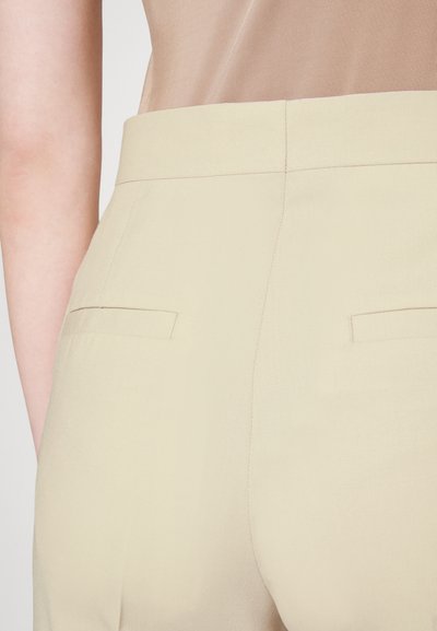 Beige trousers with a smooth texture, featuring a mid-rise waistband and two back pockets. Subtle stitching detail along the seams.