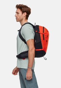Lo zaino presenta una base nera con vivaci accenti arancioni, spallacci regolabili e una cintura in vita imbottita per supporto. Design elegante con cerniere.