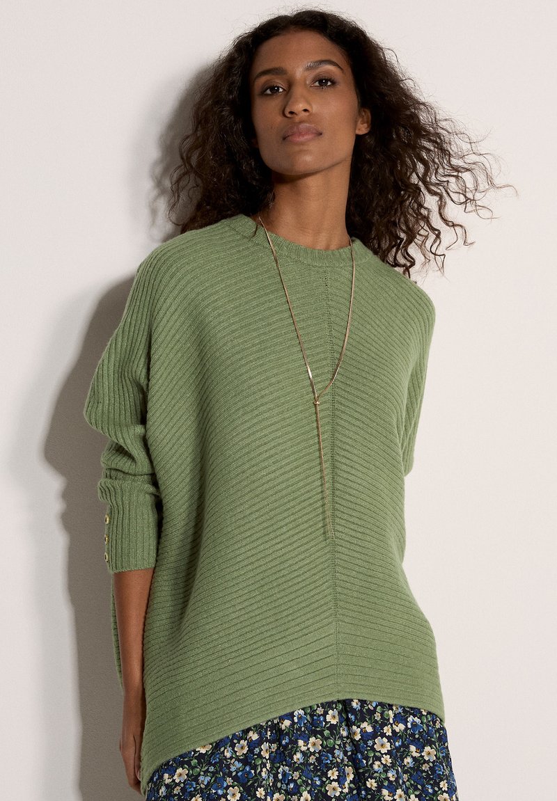Pull côtelé vert avec un large col et une coupe légèrement oversize, doté d'accents de boutons sur les manches et d'un motif texturé subtil.
