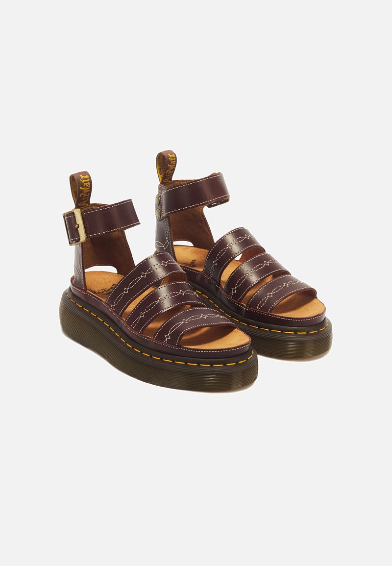 Pair of dark brown leather sandals with thick soles, wide straps, ankle buckle closures, and yellow stitching detail.