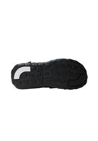 Black athletic shoe outsole featuring a textured, patterned grip with a white accent stripe and a branded logo in the center.