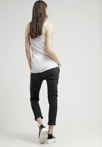 Černé denimové džíny s tapered střihem, s opotřebovanými detaily, s ohrnutými lemy, spárované s bílým topem bez rukávů a černými slip-on botami.