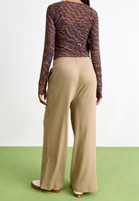 Långärmad topp med mörk bas och orange abstrakt mönster, kombinerad med beiga, vida ribbade byxor med elastiskt midjeband.