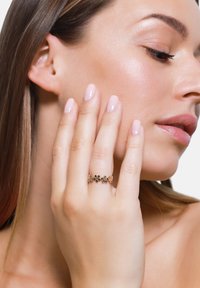 Goldring mit floralen Designs und farbigen Steinen, auf einer Hand präsentiert. Glatter Ring und polierte Oberfläche; das Modell hat einen neutralen Hintergrund.