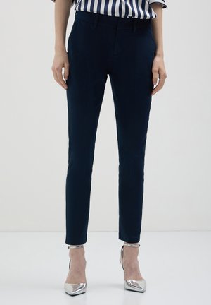 Pantaloni tailored blu navy con una vestibilità slim, caratterizzati da una superficie liscia, tasche frontali e passanti per cintura, abbinati a scarpe con tacco alto in argento.