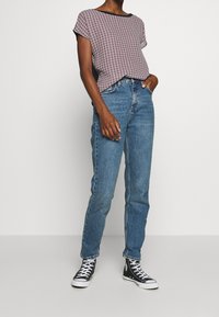 Röd och marinblå mönstrad kortärmad topp i kombination med ljusblå raka jeans och svarta högstövlade sneakers.