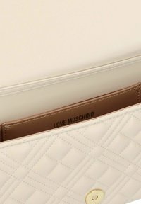 Cream quilted handbag with gold hardware, featuring a smooth texture and embossed brand name inside. Flap closure design.