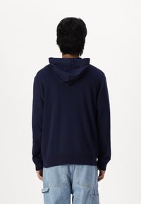 Sudadera azul marino con capucha ajustable, mangas largas y corte relajado, hecha de una tela suave con una textura lisa.