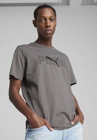 Grå bomuld t-shirt med en sort trykt "PUMA" logo henover brystet, rund halsudskæring, korte ærmer og afslappet pasform.