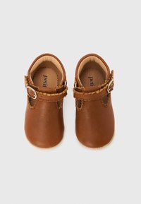 Ζευγάρι μικρά καφέ δερμάτινα παιδικά παπούτσια με λουράκια με αγκράφα, γαζωμένες άκρες και μαλακή μπεζ επένδυση σε λευκό φόντο.