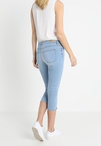 Pantalons capri en denim bleu clair à coupe slim, taille mi-haute et ourlet retroussé. Comprend deux poches arrière et une étiquette à la taille.