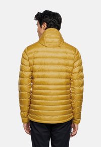Gelbe Puffjacke mit Kapuze, im gesteppte Design und strukturierter Oberfläche. Die Jacke hat eine lockere Passform und elastische Bündchen.