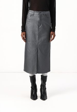 Femme portant une jupe midi taille haute gris métallisé avec une fente devant, associée à des chaussettes blanches et des bottines noires à bout pointu.
