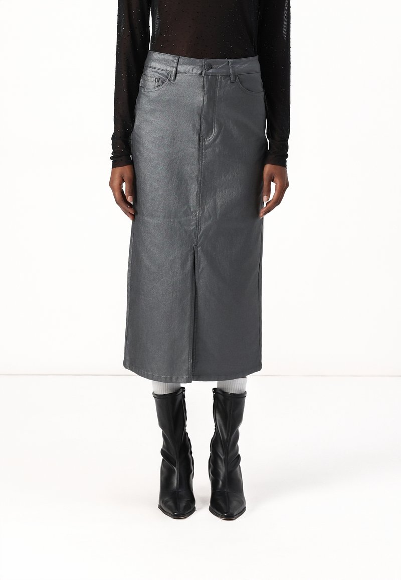 Femme portant une jupe midi taille haute gris métallisé avec une fente devant, associée à des chaussettes blanches et des bottines noires à bout pointu.