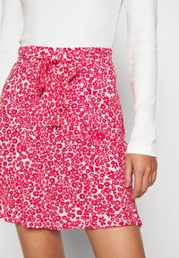 Jupe florale blanche avec motif rouge, dotée d'une taille à nouer, d'un ourlet évasé et d'un tissu léger. Haut à manches longues avec texture côtelée.