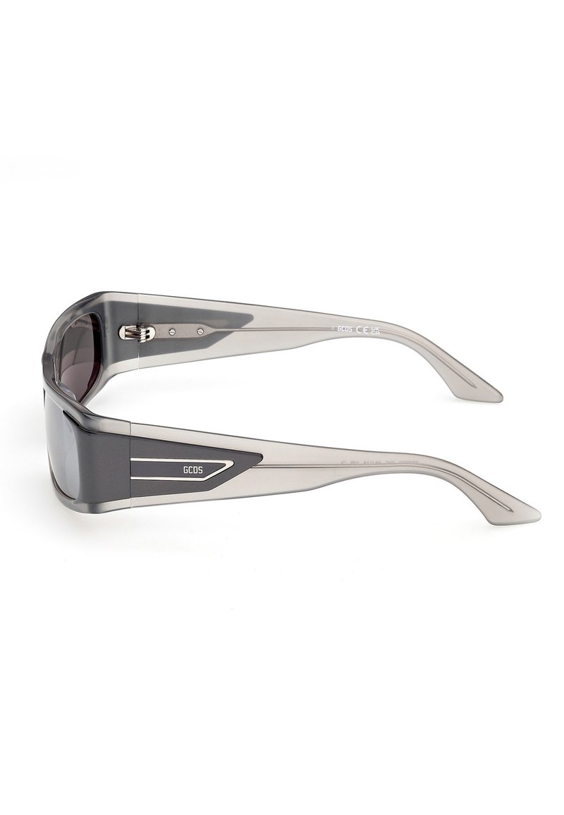 Transparante grijze rechthoekige zonnebril met donkere glazen en GCDS-logo op de pootjes, zijaanzicht op een witte achtergrond.