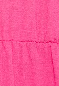 Tessuto rosa brillante texturizzato con una cucitura orizzontale e dettagli arricciati che creano leggere pieghe.
