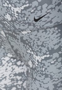 Szare legginsy sportowe z cyfrowym wzorem w odcieniach szarości i bieli, z czarnym logo Nike w pobliżu pasa.