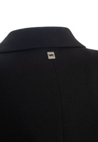 Abito nero con colletto a punta. Un'etichetta argentata con il testo "Mango" è visibile sul retro, evidenziando il dettaglio del marchio.