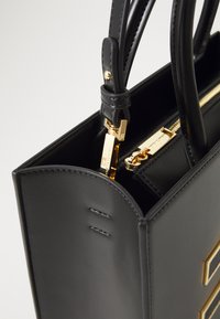 Black leather handbag with a structured design, featuring a gold zipper and hardware accents, handles, and an open top edge detail.
