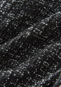 Tissu noir texturé avec des éclats blancs, présentant un design en côtes. Le matériau semble doux avec un léger éclat, capturant les variations de lumière.