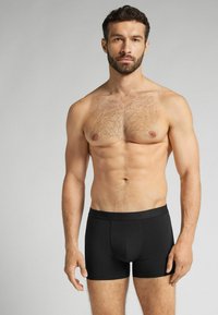 Svarta åtsittande boxershorts i elastisk tyg, med en mjuk midjeband och slät textur, bärs av en manlig modell med muskulös kropp.