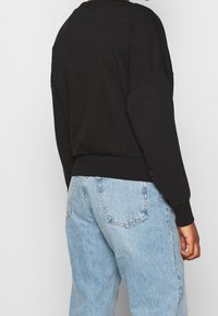Sweat-shirt noir avec épaules tombantes, poignets et ceinture côtelés, assorti à un jean en denim bleu clair avec poches arrière.