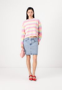 Multikleurige, fuzzy gebreide trui met roze, gele en blauwe strepen, gecombineerd met een lichtblauwe denimrok, een roze handtas en rode hoge hakken.