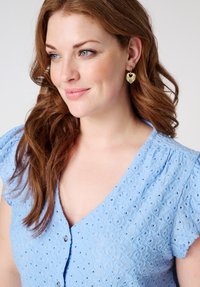 Blouse bleu clair avec un motif texturé et brodé, à manches courtes bouffantes et décolleté en V, avec une fermeture à boutons sur le devant.