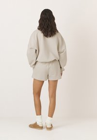 Jasno beżowy zestaw składający się z bluzy i szortów, wykonany z miękkiego, gładkiego materiału. Posiada luźny krój, z mankietami rękawów oraz szortami, w połączeniu z jasnymi skarpetkami i butami.