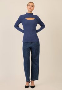 Maglione a coste blu navy con colletto alto e dettaglio a intaglio, abbinato a jeans blu con accenti a motivo sottile e tacchi neri.