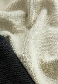 Puuvillasekoitekangas, jossa on vaaleanbeige rakenne mustan kiinteän osan rinnalla, esittelee sileän, neulotun pinnan ja pehmeän roolan.