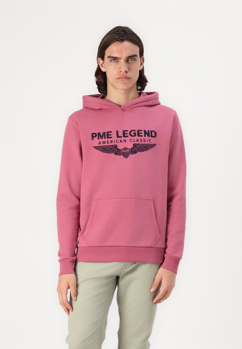 Różowa bluza z kapturem z przednią kieszenią, z dużym czarnym napisem "PME LEGEND AMERICAN CLASSIC" oraz graficznym motywem skrzydeł; materiał bawełniany, luźny krój.