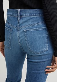 Smala blå denimjeans med hög midja, med två bakfickor och en blekt textur. Tygdet verkar mjukt och flexibelt.