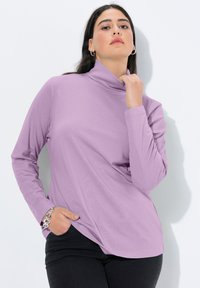 Rolák s dlouhým rukávem v světle levandulové barvě, vyrobený z hladké látky, s volným střihem a zaobleným lemem, doplněný černými kalhotami.