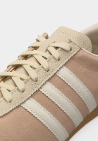 Κοντινό πλάνο μπεζ πάνινης μπότες από σουέντ με κρεμ κορδόνια και τρεις λευκές ρίγες στο πλάι.